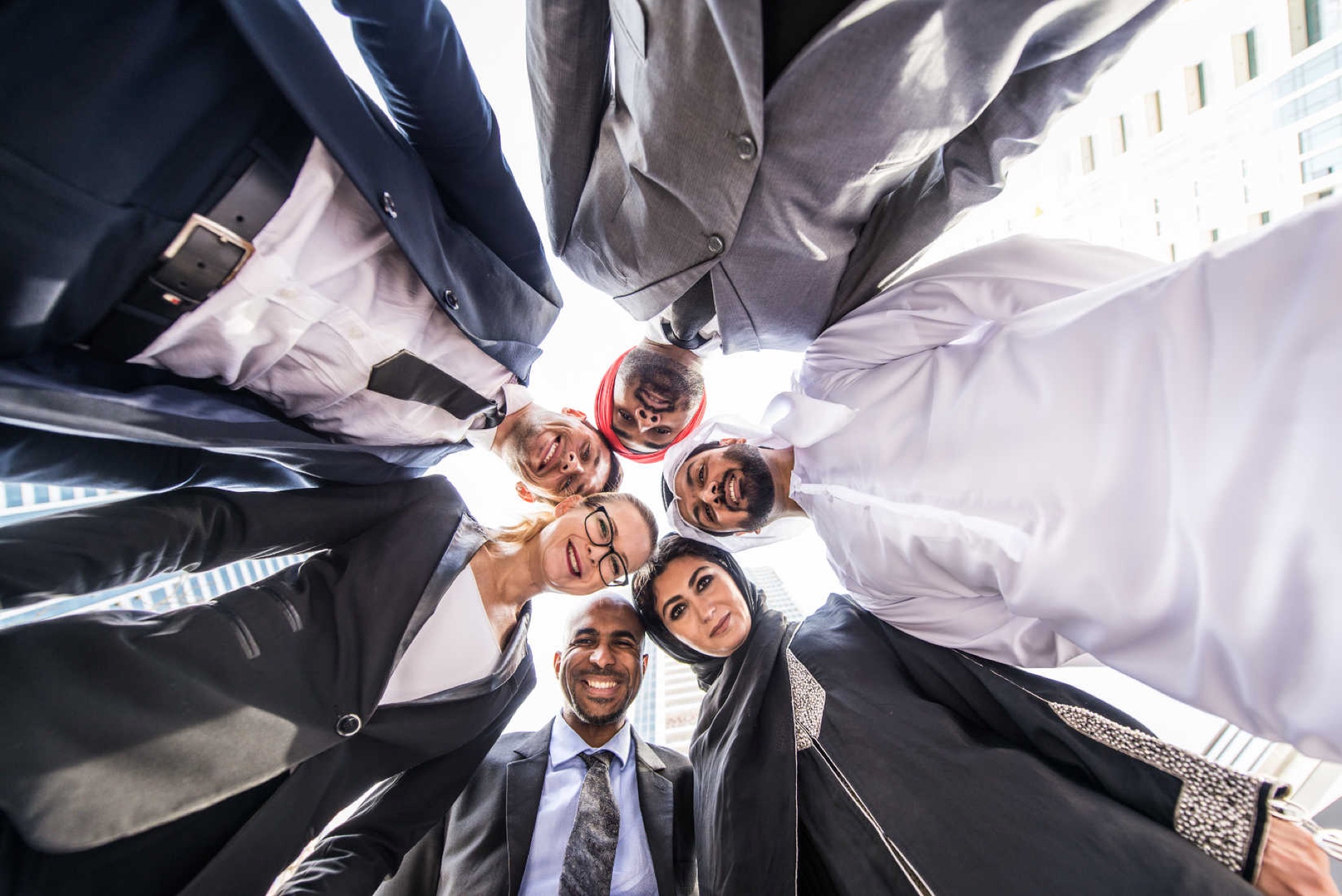 Diverse group of business professionals in a huddle viewed from below, with Dubai high-rises behind