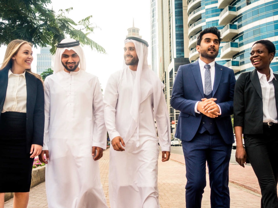 Diverse group of five professionals including two Emirati men in kanduras walking together on a Dubai street