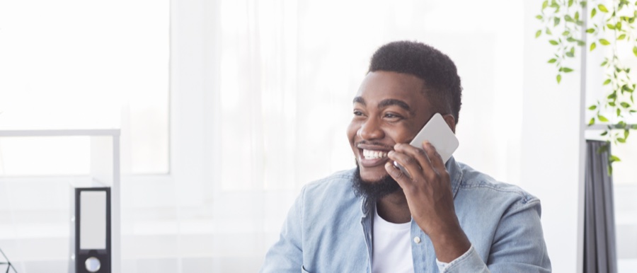 Smiling young man in denim shirt making a phone call in a bright office with houseplants